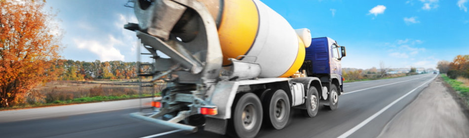 Concrete mixer truck driving fast on the countryside road with trees against blue sky with clouds