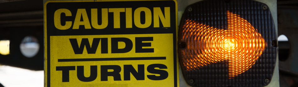 18-Wheeler Caution Wide Turns Sign with Lighted Arrow. Sign is on the undercarriage of a trailer on a big rig truck.