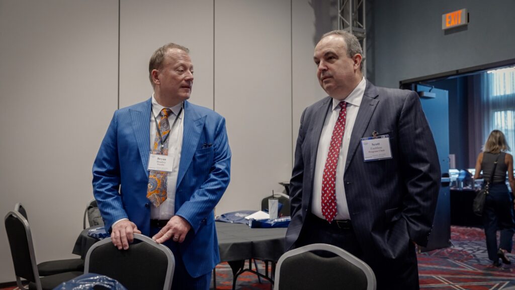 Scott Faultless walks and talks with a man in a blue suit at seminar