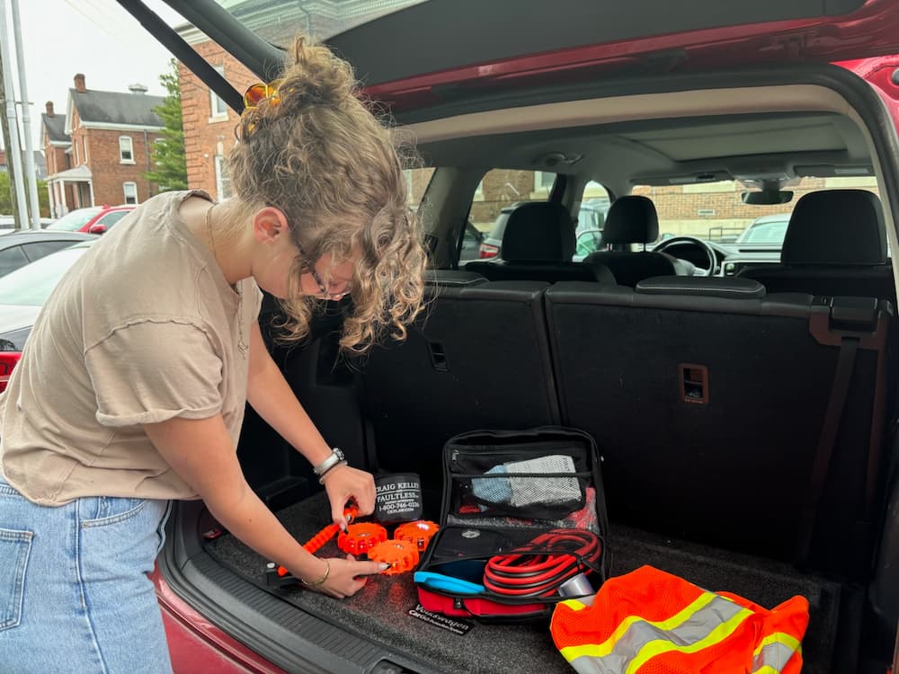 A woman organizes safety gear in the trunk of a car, preparing for a road trip.